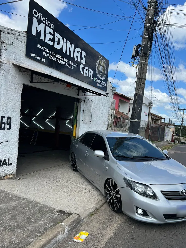 Fachada da Medinas Car com a placa da oficina e um sedan prata estacionado em frente à entrada