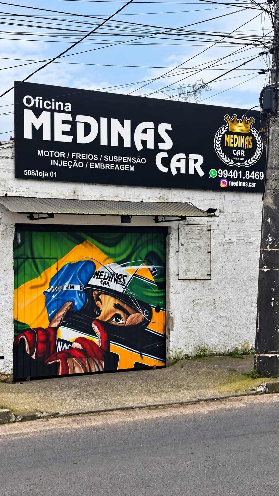Fachada da Medinas Car, em Viamão, com a placa da oficina e o portão com grafite de piloto de automobilismo